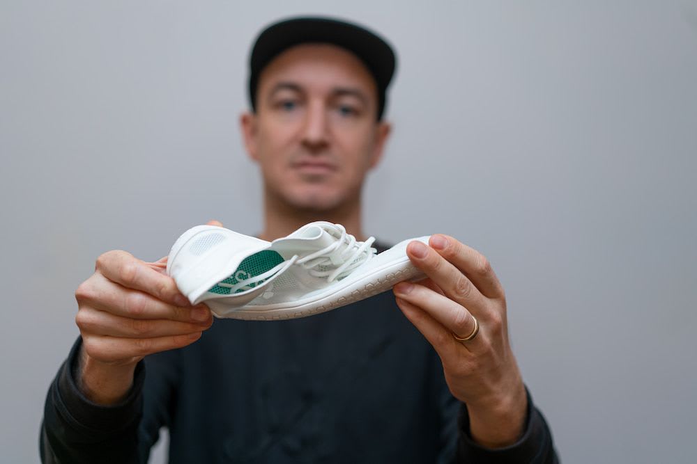 A man holding a thin soled white shoe and twisting it to demonstrate movement 