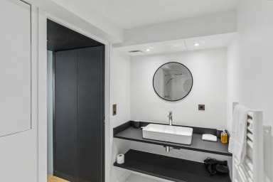 Salle de bain lumineuse avec miroir rond, serviettes et accessoires soignés.