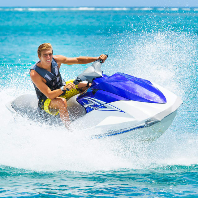 Man riding a blue and white jet ski on a clear tropical ocean