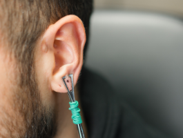 Nahaufnahme eines männlichen Ohrs mit Daith-Piercing, in das ein Werkzeug zur Kontrolle oder Anpassung des Piercings eingesetzt ist, Fokus auf Ohr und Piercingstelle.