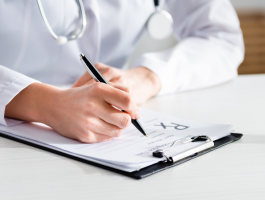 Ärztin oder Arzt schreibt ein Rezept auf einem Klemmbrett, daneben stehen medizinische Cannabisprodukte und CBD-Öle auf einem Tisch – Symbolbild für Cannabisverordnung und telemedizinische Beratung.