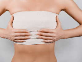 Frau mit bandagierter Brust nach einer Brustverkleinerung, Hände stützen den Oberkörper. Symbolbild für Mammareduktion, Heilungsphase nach OP und medizinisch begründete Brustoperation.