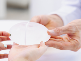 Ärztin zeigt Patientin ein Brustimplantat bei Beratung zur gewebeschonenden Brustvergrößerung in einer plastisch-chirurgischen Praxis.