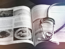Stethoskop liegt auf einem aufgeschlagenen medizinischen Fachbuch mit Abbildungen und Texten zu Herzerkrankungen.