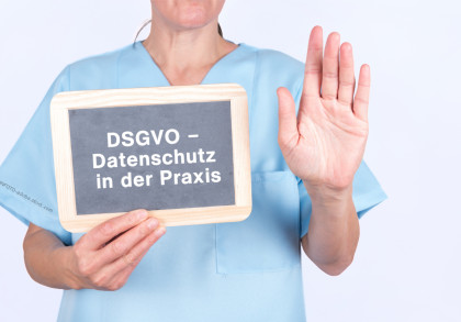Eine Person in blauer medizinischer Kleidung hält ein Schild mit der Aufschrift "DSGVO - Datenschutz in der Praxis" in der linken Hand und hebt die rechte Hand zur Seite.