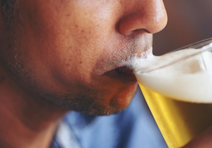 Eine Nahaufnahme einer Person, die ein Glas Bier trinkt, wobei Schaum auf der Oberlippe zu sehen ist.