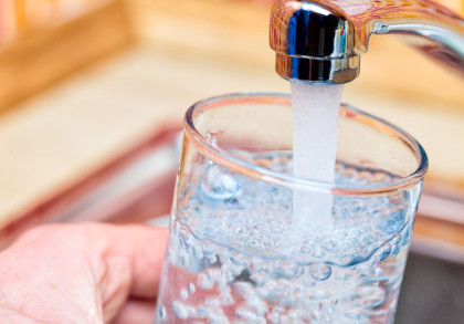 Eine Hand hält ein Glas unter einen laufenden Wasserhahn, das Glas wird mit Wasser gefüllt.