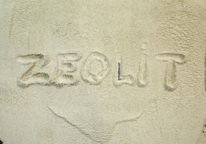 Das Bild zeigt das Wort "ZEOLIT", das in hellem, sandfarbenem Pulver geschrieben ist.
