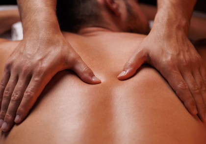 Nahaufnahme von Händen, die eine Rückenmassage geben. Eine Person liegt auf dem Bauch und erhält eine Massage, die Hände drücken sanft auf die Haut entlang der Wirbelsäule.
