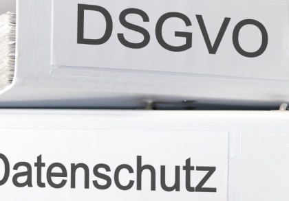 Porträt eines lächelnden Mannes mittleren Alters in einem dunklen Anzug mit weißem Hemd und blau-gemusterter Krawatte. Er hat kurzes, dunkles Haar und steht vor einem unscharfen Hintergrund, der weiche, grüne und graue Töne aufweist.
