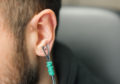 Nahaufnahme eines männlichen Ohrs mit Daith-Piercing, in das ein Werkzeug zur Kontrolle oder Anpassung des Piercings eingesetzt ist, Fokus auf Ohr und Piercingstelle.