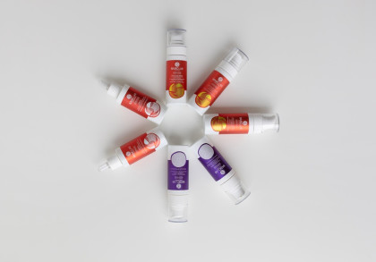 Mehrere Retinol-Seren in roten und violetten Spendern liegen kreisförmig auf weißem Hintergrund.