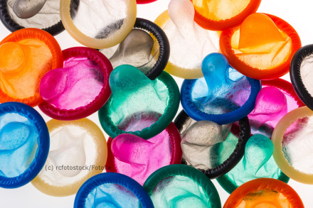 Ein Haufen bunter Kondome in verschiedenen Farben, wie Orange, Blau, Grün, Pink und Gelb, verteilt auf einer weißen Oberfläche.