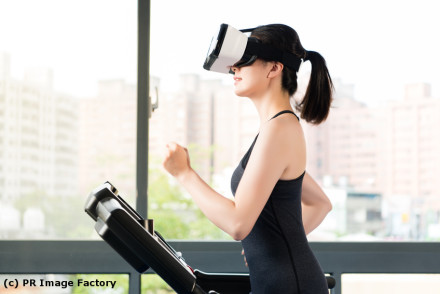 Eine Frau läuft auf einem Laufband und trägt eine Virtual Reality-Brille. Im Hintergrund sind unscharf Gebäude zu sehen. (c) PR Image Factory