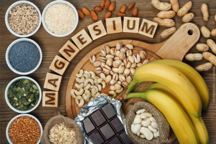 Das Bild zeigt verschiedene Lebensmittel, die reich an Magnesium sind. Dazu gehören Sonnenblumenkerne, Sesam, Mohnsamen, Kürbiskerne, Buchweizen, Haferflocken, Mandeln, Cashewnüsse, Pistazien, Erdnüsse, weiße Bohnen, dunkle Schokolade und Bananen.