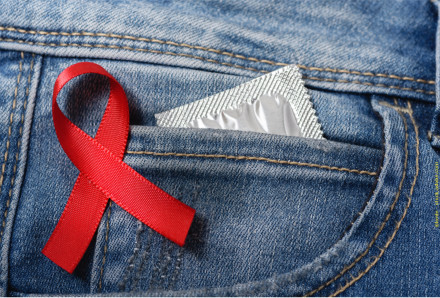 Ein rotes Band, das als Symbol für die Unterstützung der AIDS-Bekämpfung dient, ist auf eine Jeans-Tasche gesteckt. In der Tasche steckt ein silbernes Kondompäckchen.