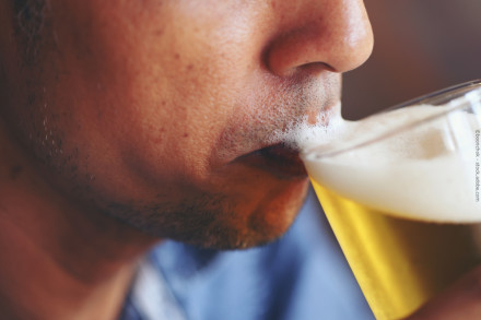 Eine Nahaufnahme einer Person, die ein Glas Bier trinkt, wobei Schaum auf der Oberlippe zu sehen ist.