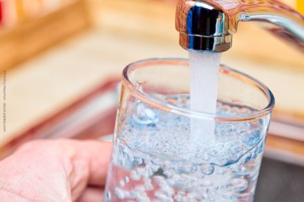 Eine Hand hält ein Glas unter einen laufenden Wasserhahn, das Glas wird mit Wasser gefüllt.