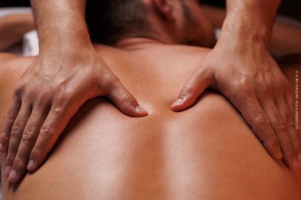 Nahaufnahme von Händen, die eine Rückenmassage geben. Eine Person liegt auf dem Bauch und erhält eine Massage, die Hände drücken sanft auf die Haut entlang der Wirbelsäule.