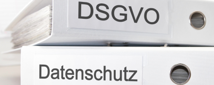 Porträt eines lächelnden Mannes mittleren Alters in einem dunklen Anzug mit weißem Hemd und blau-gemusterter Krawatte. Er hat kurzes, dunkles Haar und steht vor einem unscharfen Hintergrund, der weiche, grüne und graue Töne aufweist.