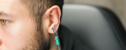 Nahaufnahme eines männlichen Ohrs mit Daith-Piercing, in das ein Werkzeug zur Kontrolle oder Anpassung des Piercings eingesetzt ist, Fokus auf Ohr und Piercingstelle.