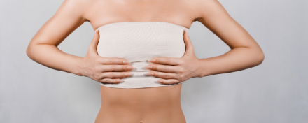 Frau mit bandagierter Brust nach einer Brustverkleinerung, Hände stützen den Oberkörper. Symbolbild für Mammareduktion, Heilungsphase nach OP und medizinisch begründete Brustoperation.