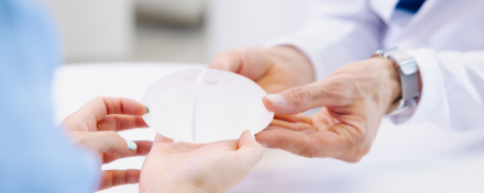 Ärztin zeigt Patientin ein Brustimplantat bei Beratung zur gewebeschonenden Brustvergrößerung in einer plastisch-chirurgischen Praxis.