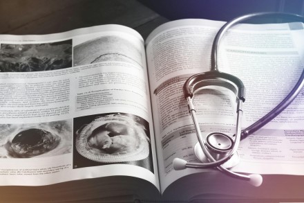 Stethoskop liegt auf einem aufgeschlagenen medizinischen Fachbuch mit Abbildungen und Texten zu Herzerkrankungen.
