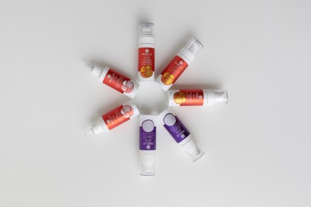 Mehrere Retinol-Seren in roten und violetten Spendern liegen kreisförmig auf weißem Hintergrund.