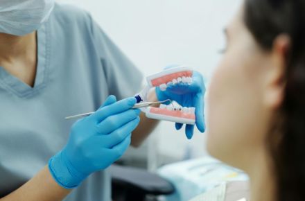 Ein Kieferorthopäde zeigt einer Patientin ein Modell mit fester Zahnspange.