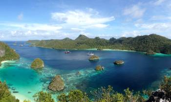 a small island in the middle of a body of water with Raja Ampat Islands in the background
