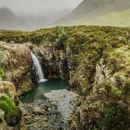 Enchanting Travels UK & Ireland Tours Waterfall in a cloudy day at the Fairy Pool trail, Isle of Skye, Scotland, UK