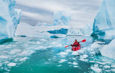 Man paddling on kayak between ice in Antractica, near Pleneau Island