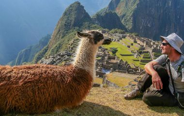 Tourist and llama sitting in front of Machu Picchu, Peru, South America