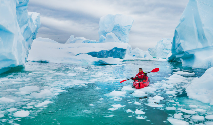 Man paddling on kayak between ice in Antractica, near Pleneau Island