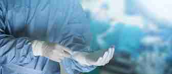 A surgeon wearing a blue surgical gown, mask, and gloves is preparing in the foreground, while an operating room with blurred figures and surgical equipment is visible in the background under bright lights.
