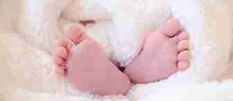 Close-up of a baby's tiny feet wrapped in a soft, white, fluffy blanket. The image conveys warmth and tenderness, highlighting the delicate and gentle nature of newborns.