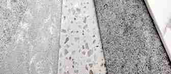 A close-up of five different concrete samples arranged side by side. The samples feature various textures and colors, ranging from light gray and speckled terrazzo in the center to darker gray and smooth finishes on either side.