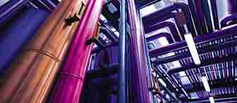 A vibrant and colorful industrial scene with tall metallic pipes in shades of purple, pink, and copper running in various directions under bright lighting. The pipes are part of a complex system, creating a visually striking and futuristic environment.