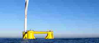 A single wind turbine with white blades and a yellow base floats on calm, blue ocean water. The sky is clear and blue, and the turbine is positioned toward the left side of the image, capturing a renewable energy solution.