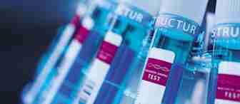 Close-up image of several test tubes with white caps and blue labels, each labeled "Biological Sample Test." The test tubes are arranged in a slanted row within a rack, and the focus is on the labels and the caps. The lighting casts a blue tint overall.