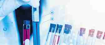 A lab technician's gloved hand holds a test tube filled with blue liquid over a rack containing multiple colored test tubes. Transparent data graphics and icons overlay the image, suggesting analysis and research activity.