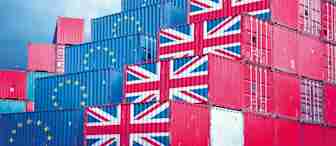 A stack of shipping containers decorated with the flags of the United Kingdom and the European Union against a cloudy blue sky. The containers are arranged in a stepped formation, with some bearing the UK flag and others the EU flag.