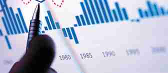 A hand holding a pen is pointing at a multi-colored graph on a screen. The graph shows various lines and bar charts, depicting data trends from 1980 to the 2000s. The main colors used are blue, red, and pink, indicating different data series.