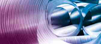 Close-up of large, coiled metal pipes arranged in a spiraling pattern. The pipes have a reflective, ribbed surface, and the lighting creates a gradient of blue and purple hues, highlighting their metallic texture. The image gives an abstract, industrial feel.