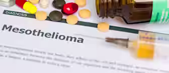 A document titled "Mesothelioma" is surrounded by various medications, including pills and capsules, and an open pill bottle. A syringe rests on the paper.
