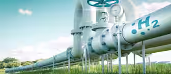 A metal pipeline marked with "H2" and a gauge is shown running through a green grassy field. Wind turbines are visible in the background under a clear blue sky, indicating renewable energy.