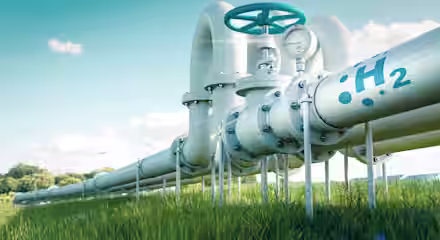 A metal pipeline marked with "H2" and a gauge is shown running through a green grassy field. Wind turbines are visible in the background under a clear blue sky, indicating renewable energy.