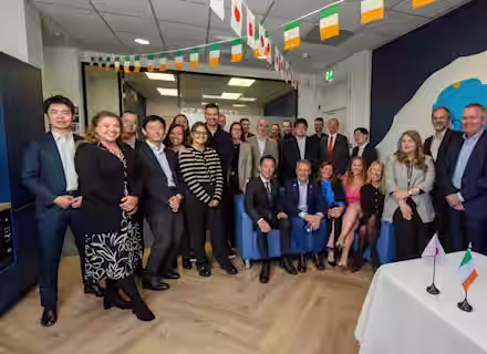 A group of people poses for a photo in an office decorated with Japanese and Irish flags; two small flags are placed on a white table in the foreground.