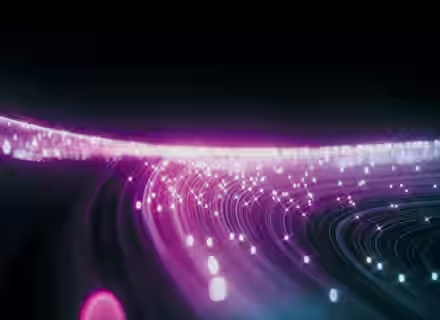 A vibrant, abstract digital artwork featuring streaks of glowing light trails in pink, purple, and blue hues against a dark background. The light trails curve and overlap, creating a dynamic and futuristic effect with scattered, sparkling particles.